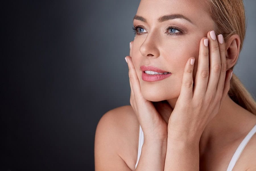 smiling woman with bare shoulders touching face. Pleased woman touching face