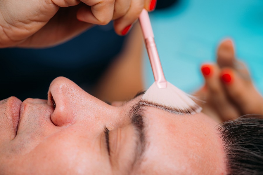 The cosmetologist applies oil (or phytic acid) to the client's face in the beauty salon. A female hands of a beautician with a brush. Facial skincare. Beautiful woman on a cosmetology procedure | Kay Dermatology in Burbank, CA
