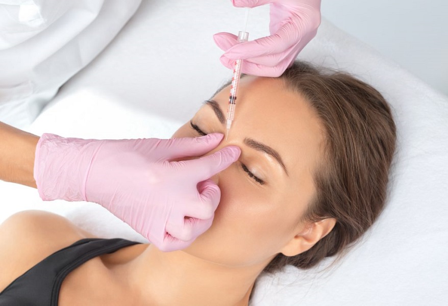Young asian woman is standing and closing her eyes while getting prick of botox injection in her brow area. Girl is frowning her forehead for Frown Lines | Kay Dermatology in Burbank, CA